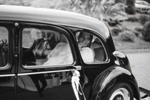 Classic vintage black car with wedding couple inside captured in black and white photography.