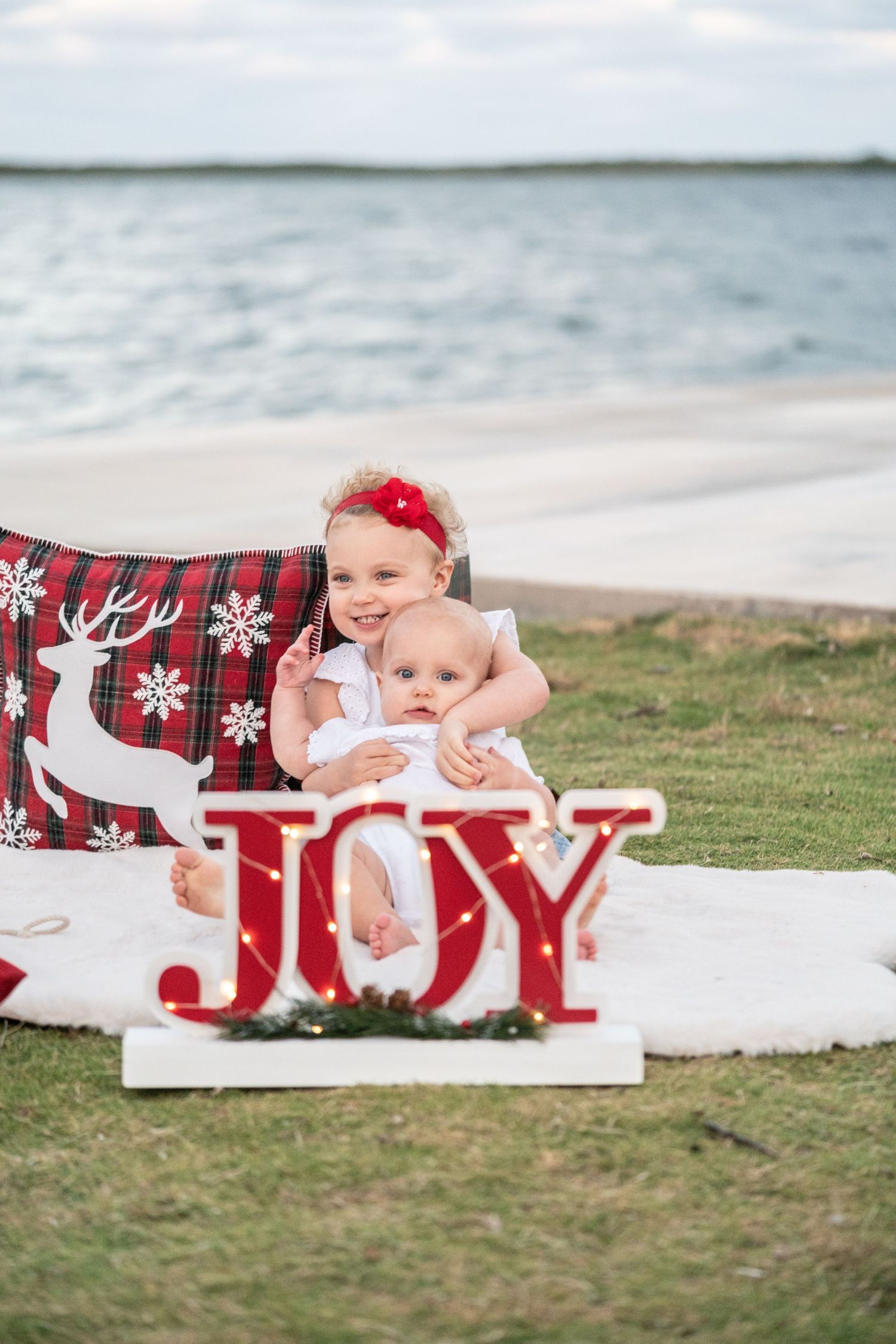 Christmas decorative JOY letters arranged on grass with beach and ocean in background.
