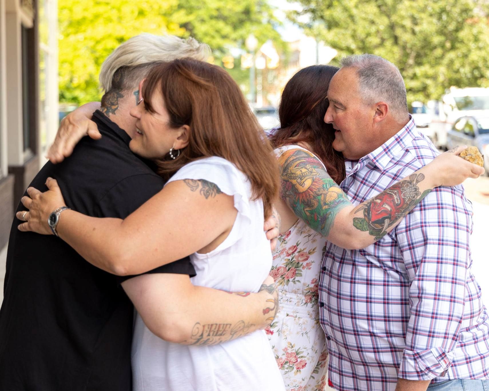 Group sharing emotional embrace outside on sunny day.
