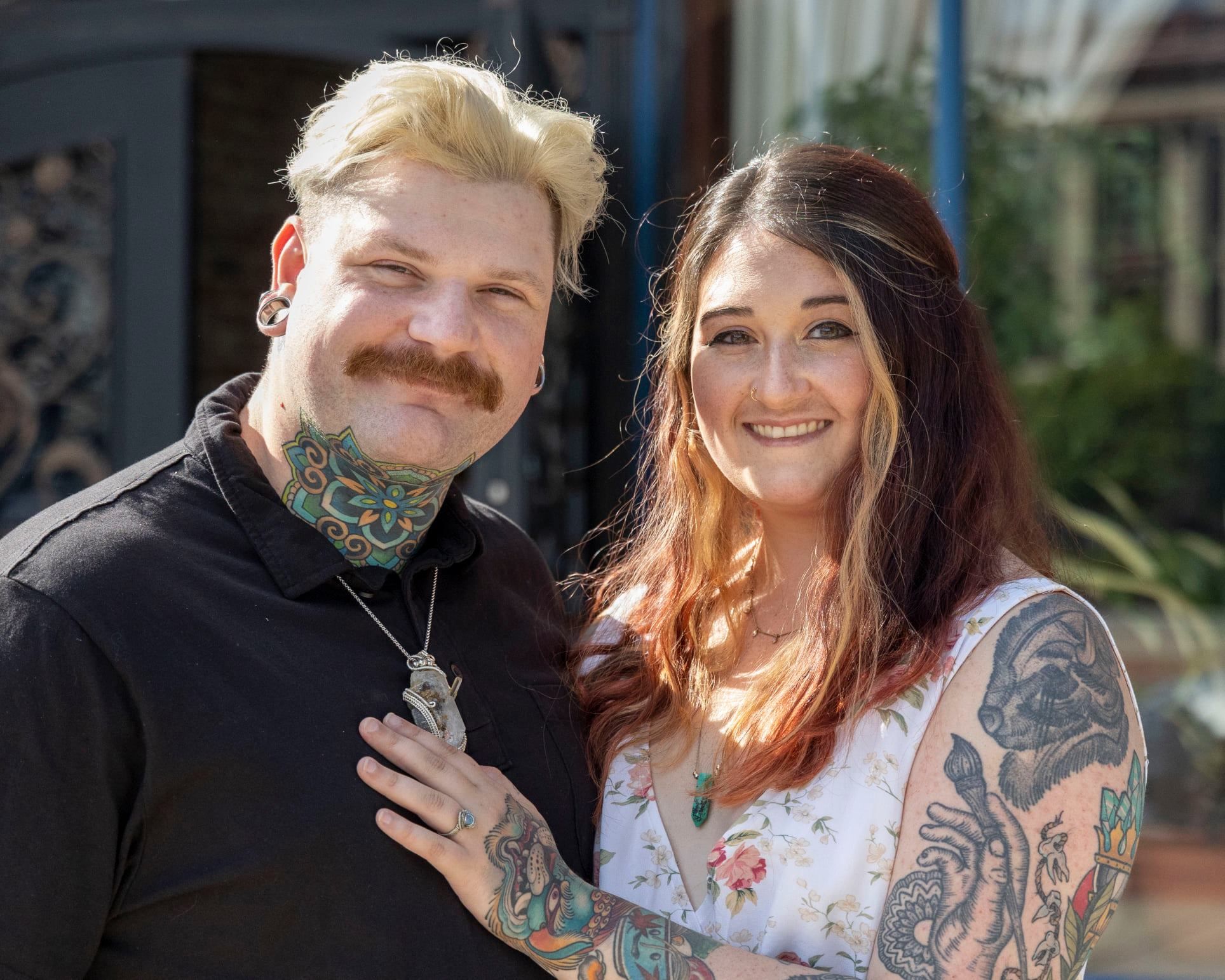 Couple with tattoos pose together in front of decorative gate.