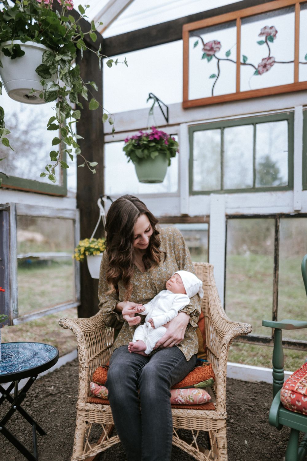 Peaceful moment in greenhouse as caregiver holds sleeping newborn in wicker chair.