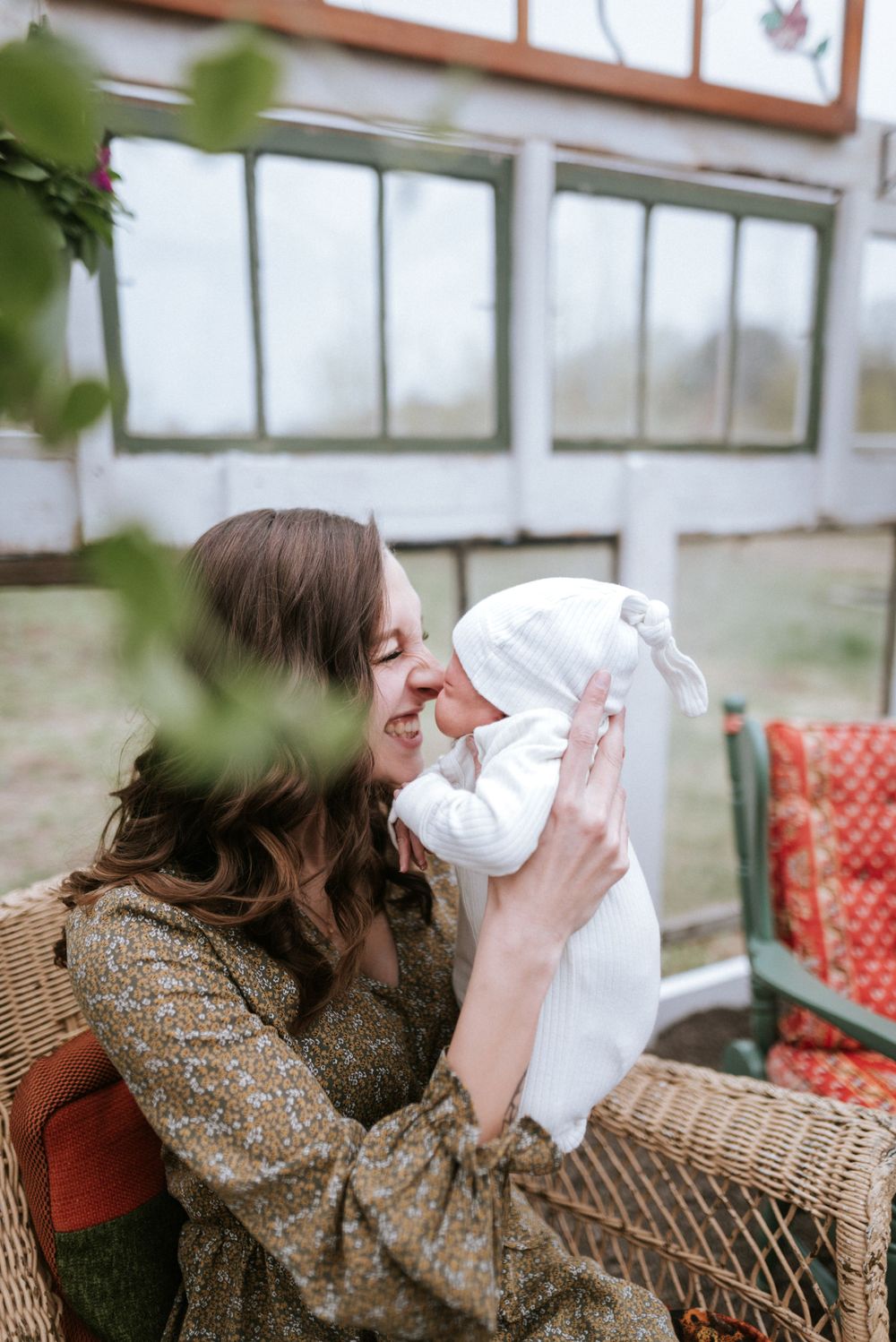 Tender moment between caregiver and newborn baby in white outfit inside bright greenhouse.