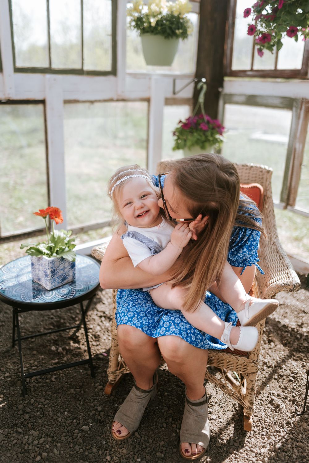 Sweet cuddles and laughter shared in a greenhouse filled with hanging plants and natural light.