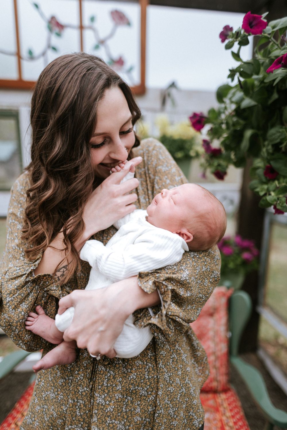A tender moment between parent and newborn baby in a sunlit greenhouse with blooming flowers.