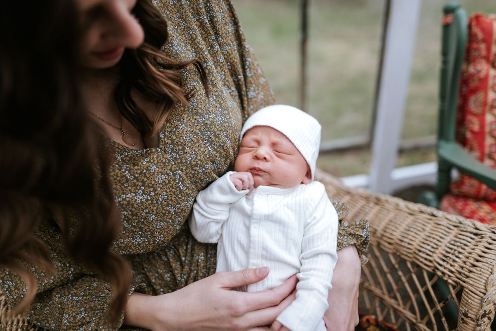 Close-up of sleeping newborn in white outfit being cradled in greenhouse setting.