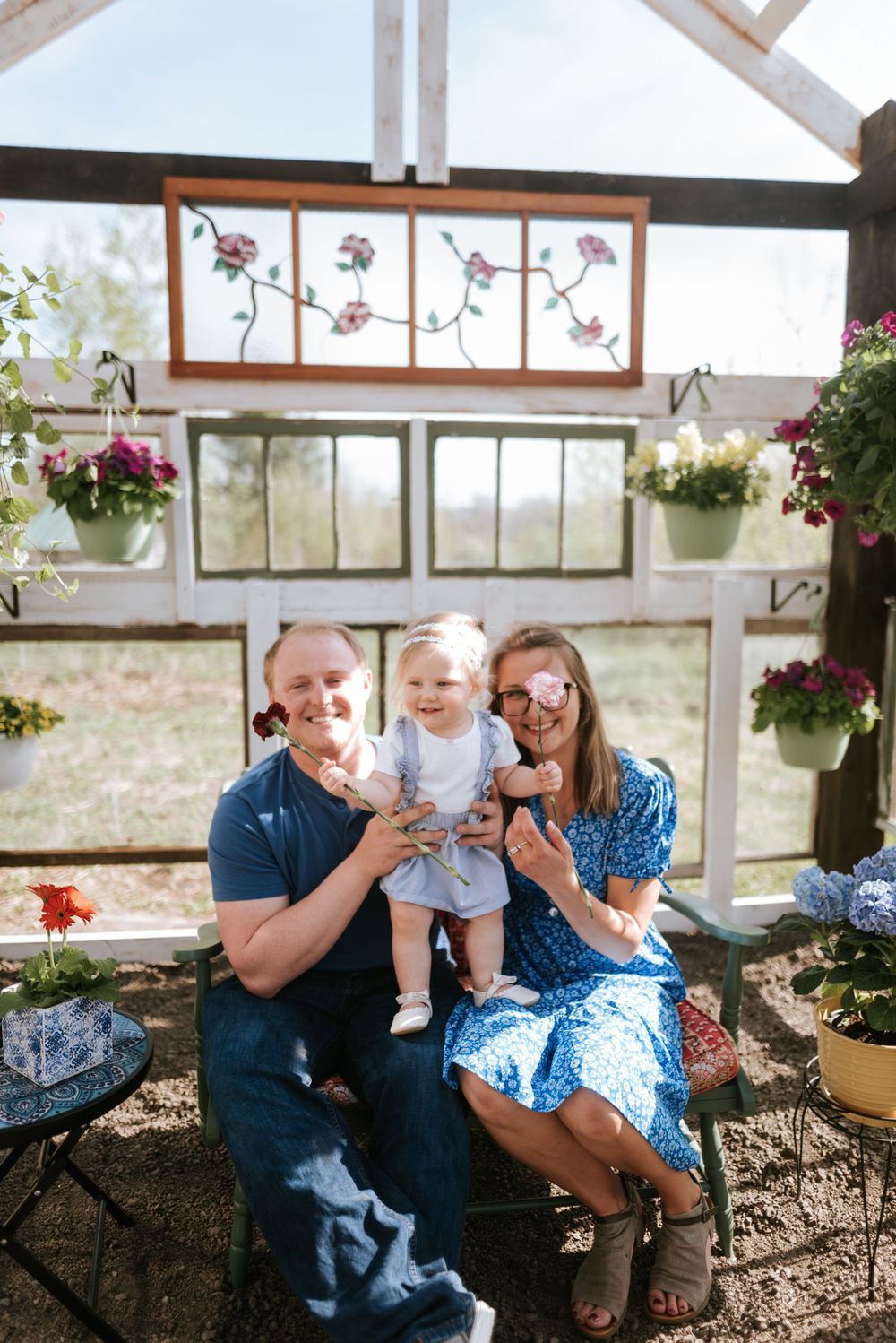 Happy family moment together in a greenhouse with hanging flower baskets and decorative windows.