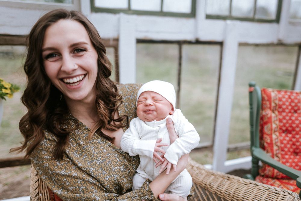 Joyful moment with newborn baby in white outfit being held in greenhouse setting.