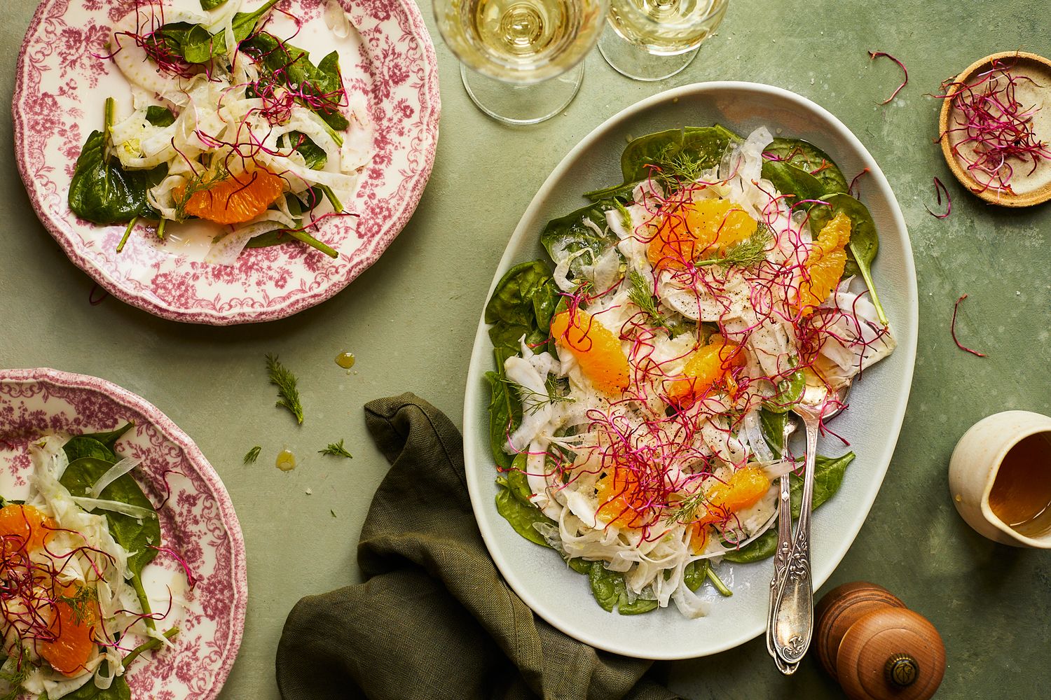 Fresh salad plates with sunny side up eggs, greens and wine glasses on sage green tablecloth.