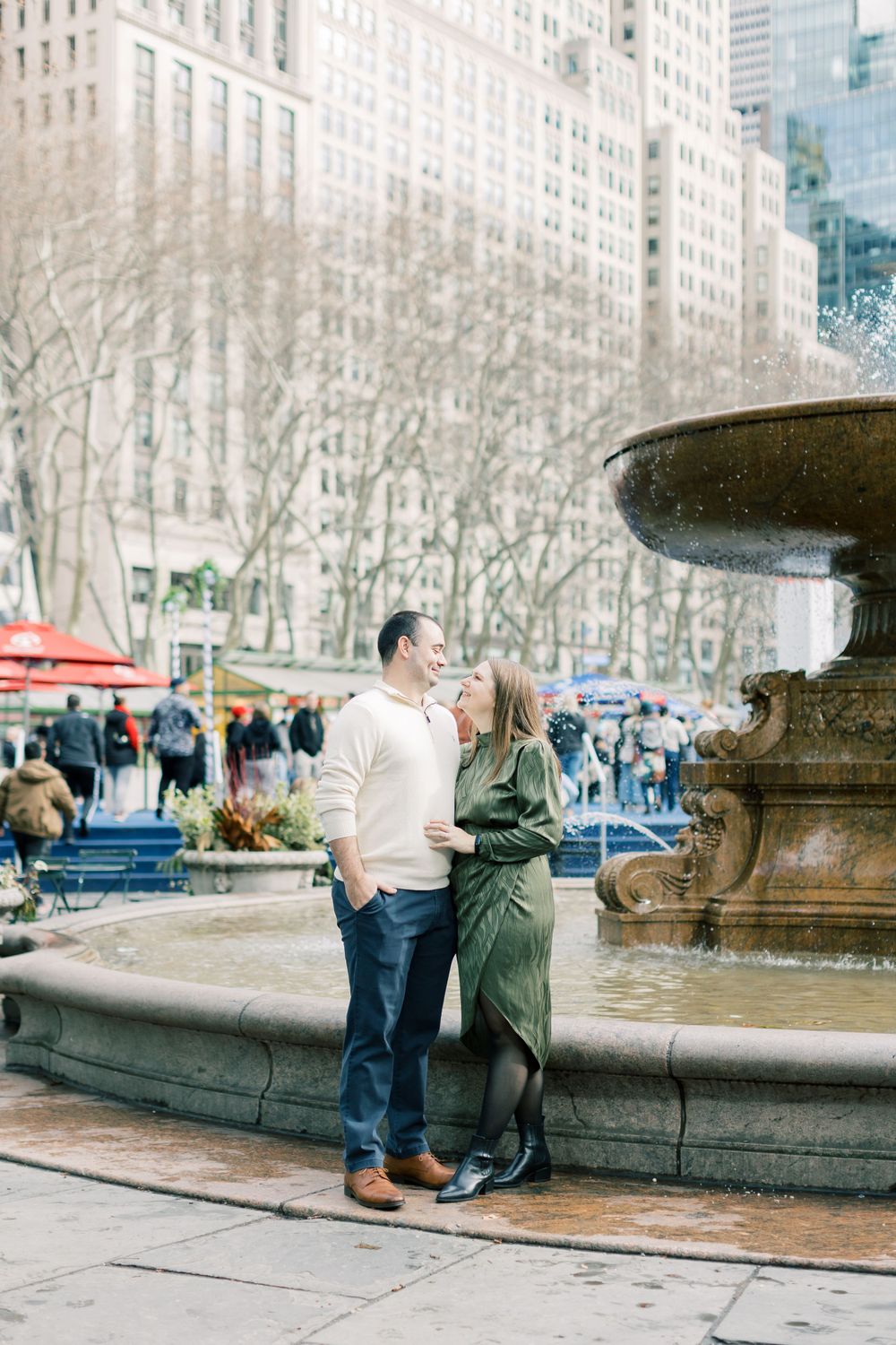 Couple standing by fountain in Bryant Park NYC during engagement photoshoot.
