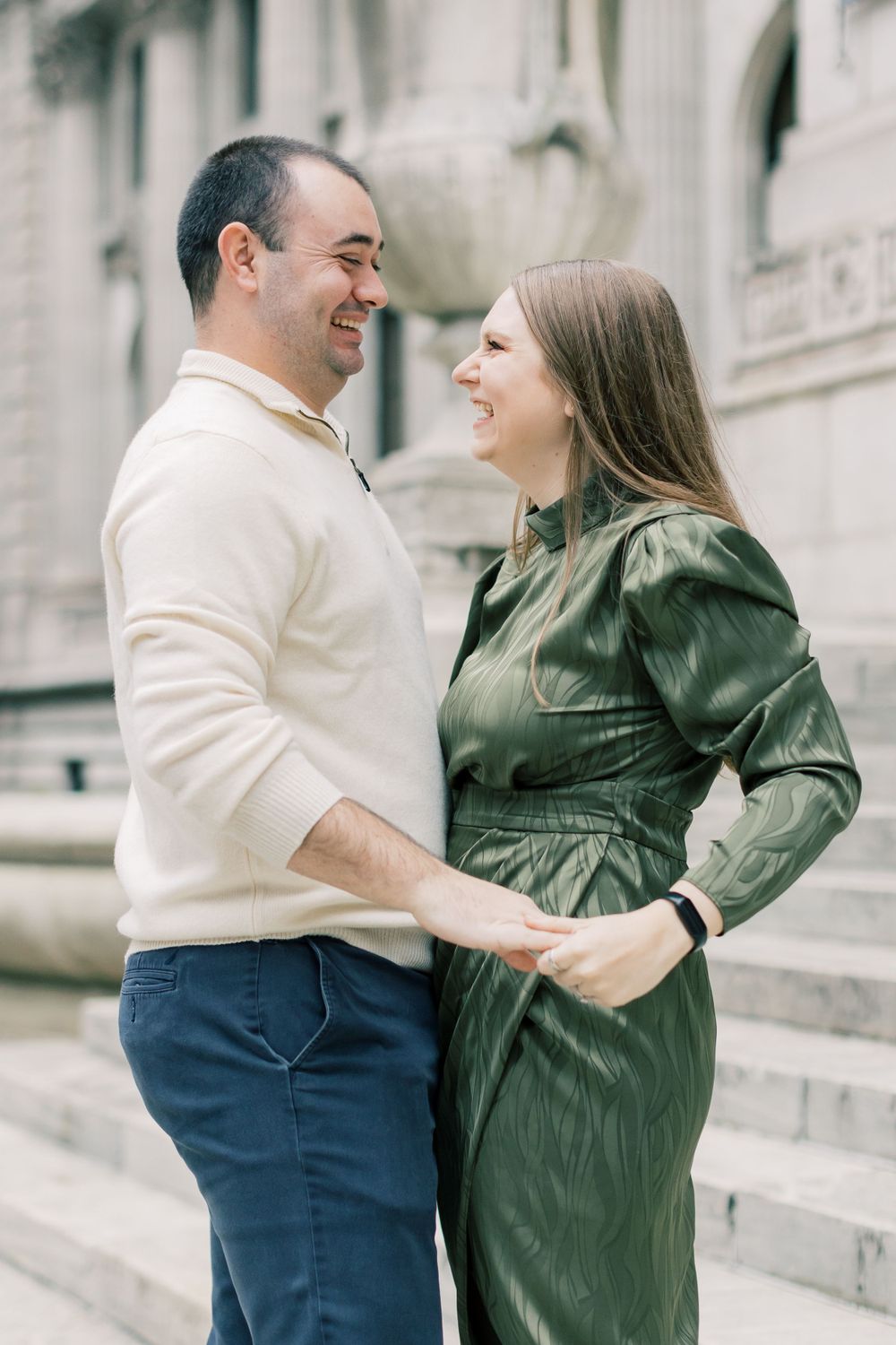 Happy couple shares a laugh while standing on marble steps in coordinated cream and green outfits.