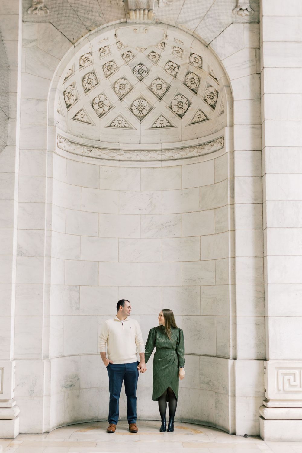 Couple stands holding hands under an ornate domed alcove in classic architecture.
