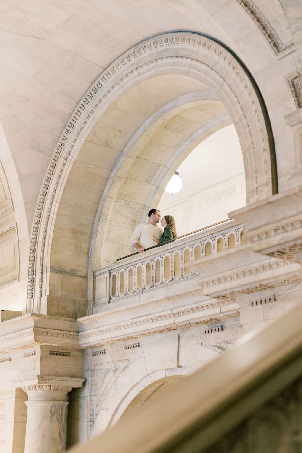 Romantic couple poses on elegant marble balcony under classical architectural arches.