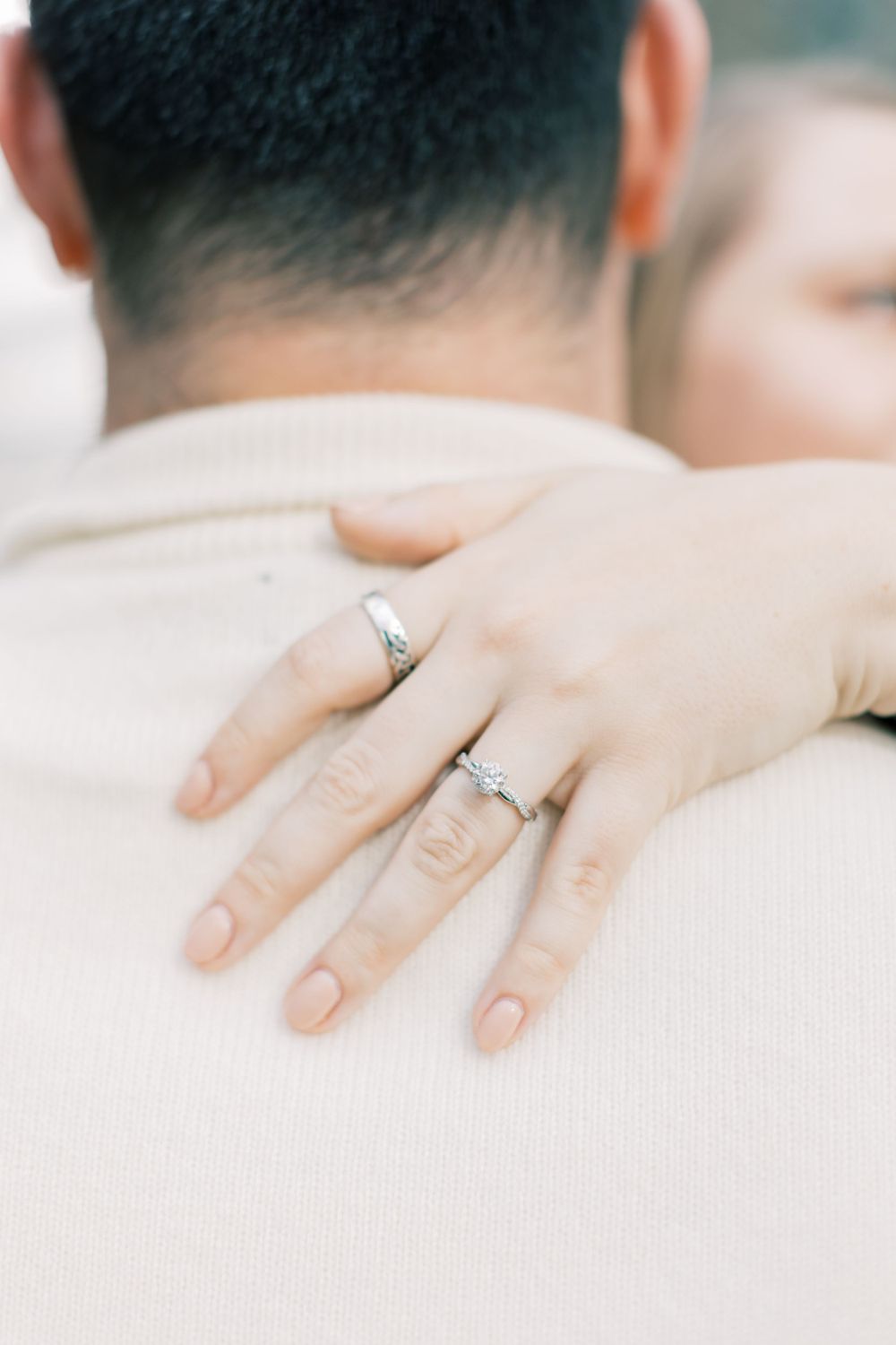 Close-up of hands with engagement rings embracing in cream sweater.