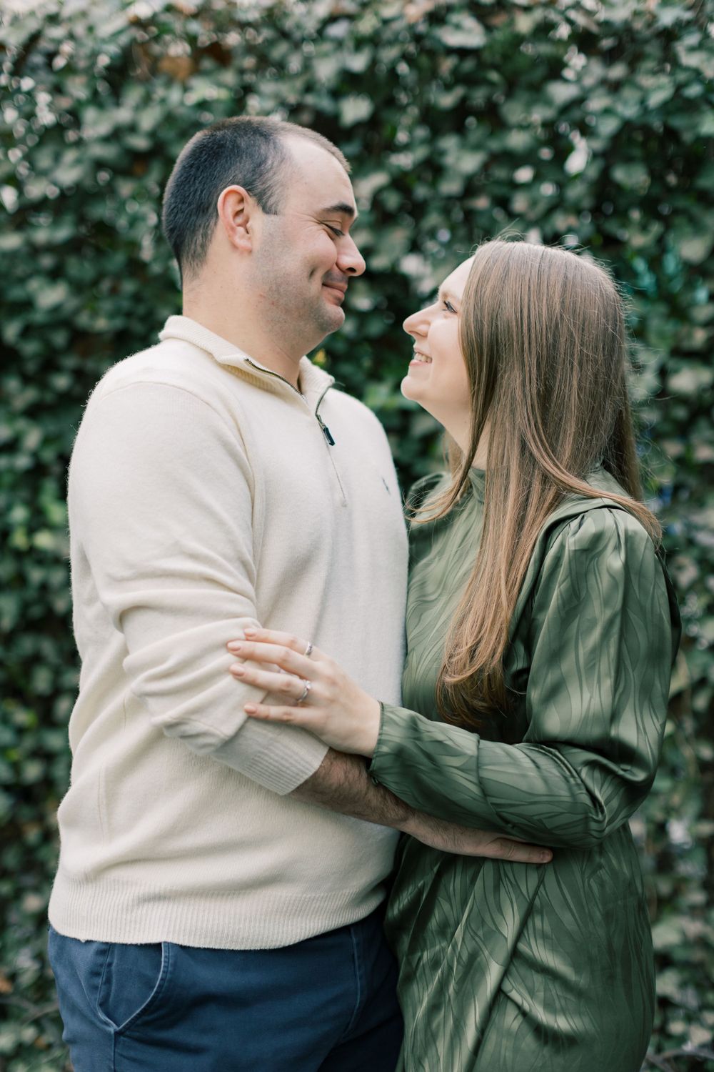 Romantic couple embracing outdoors against ivy wall background.