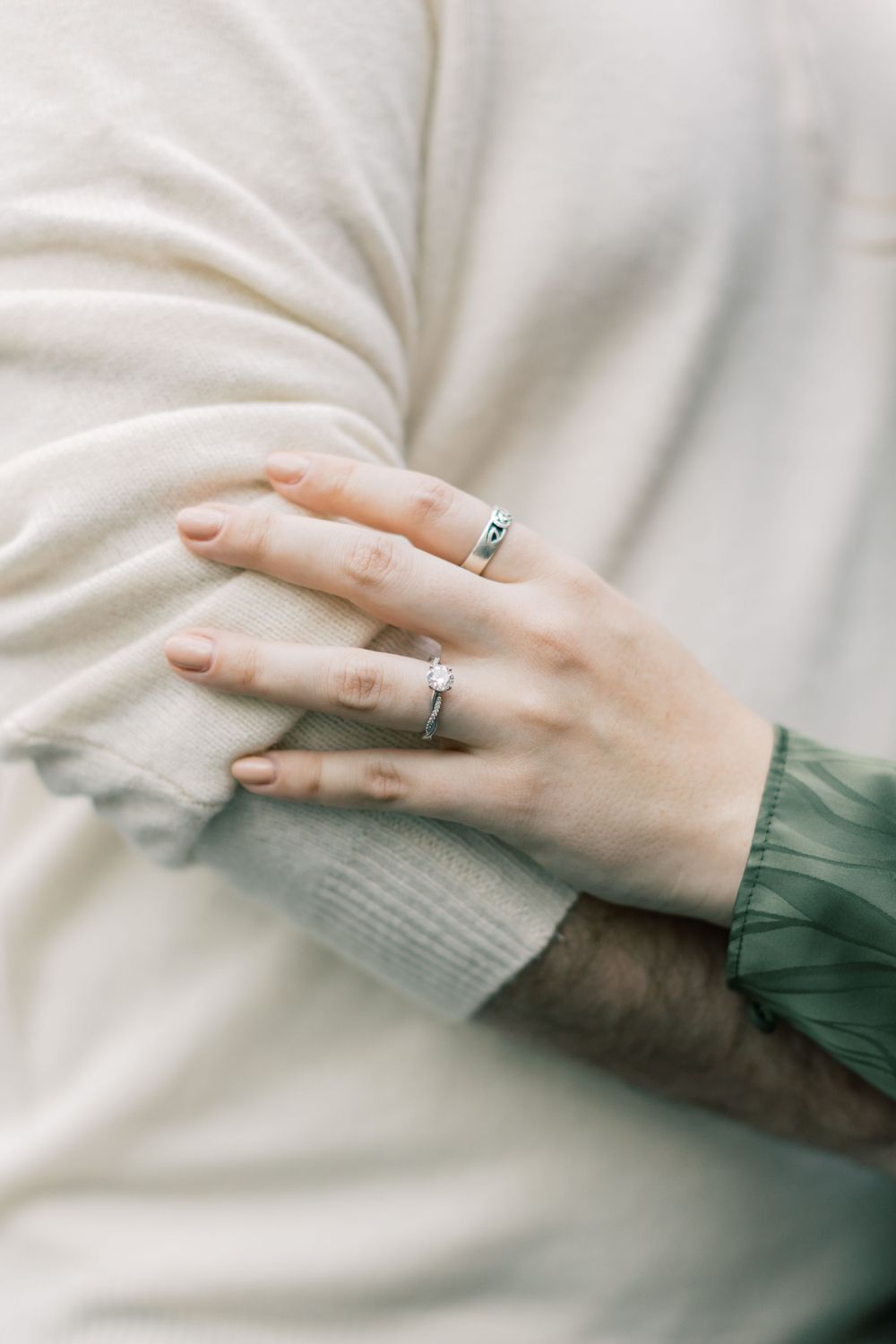 Detail shot of engagement rings against cream sweater and green sleeve.