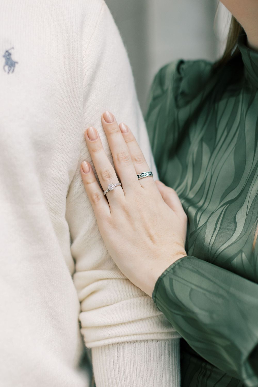 Close-up of engagement ring against cream polo shirt and green jacket.