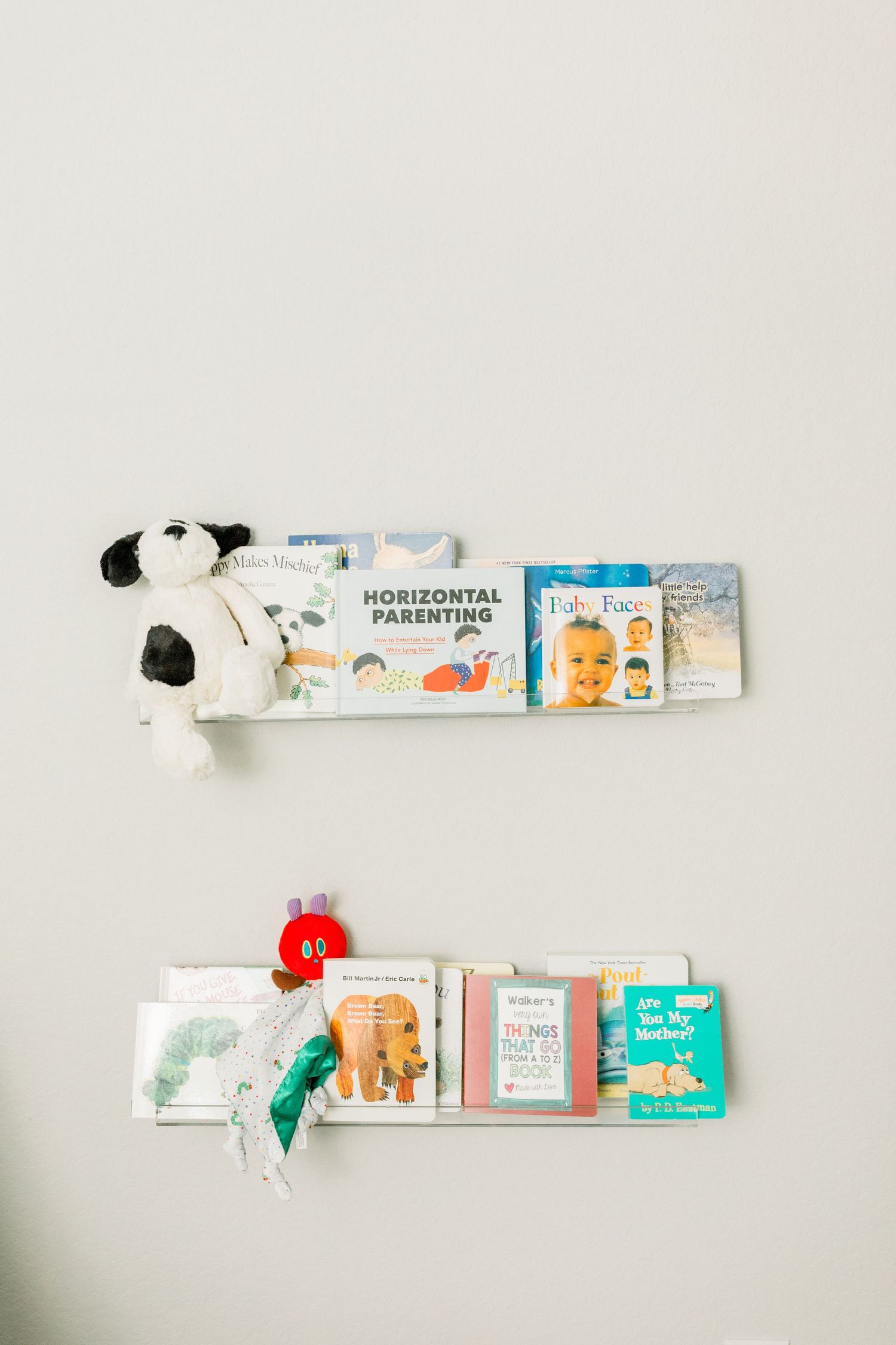 Two floating wall shelves displaying children's books and stuffed animals in a minimalist nursery setting.