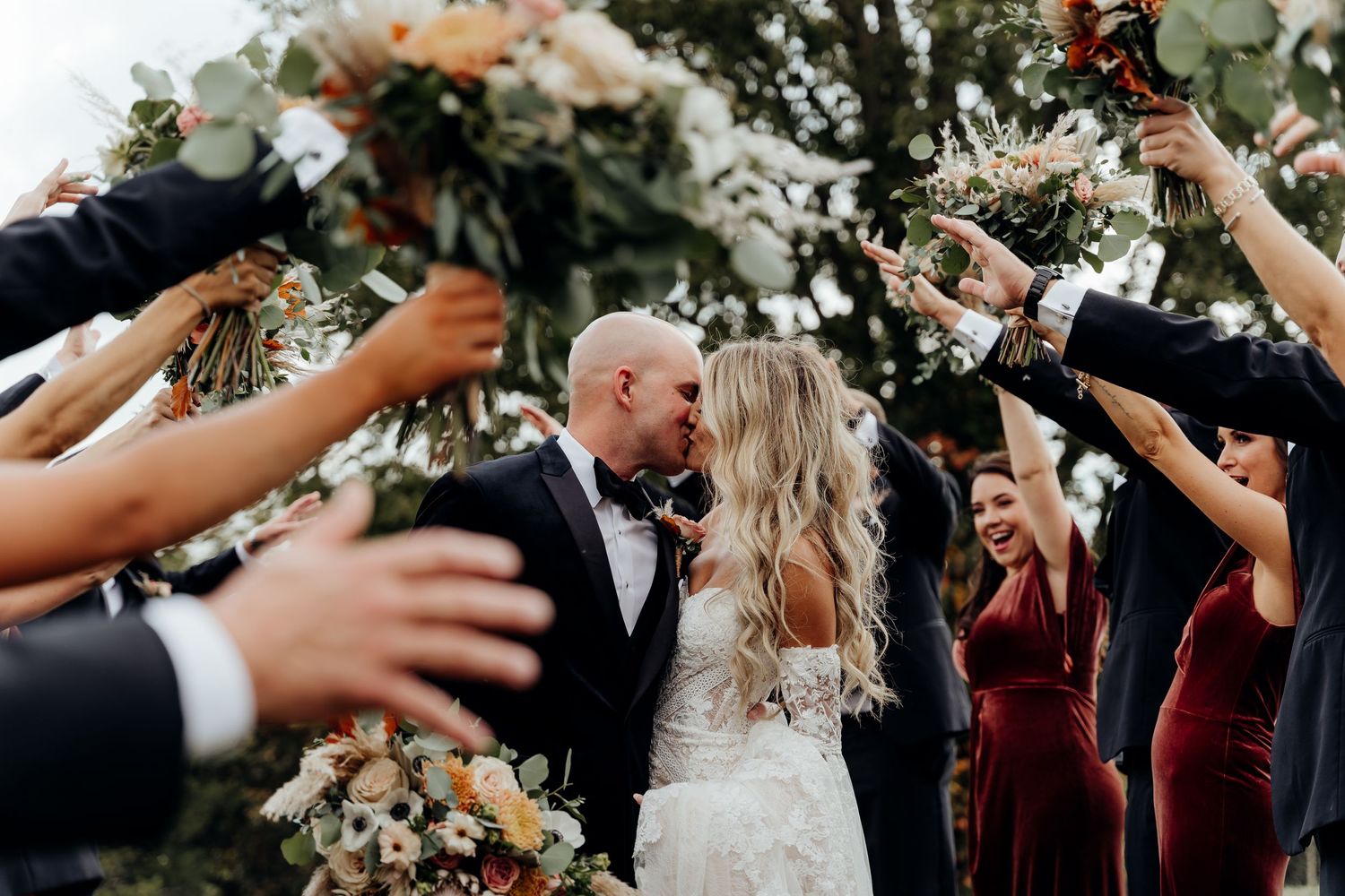 Bride and groom kissing, in between bridal party holding up flowers.