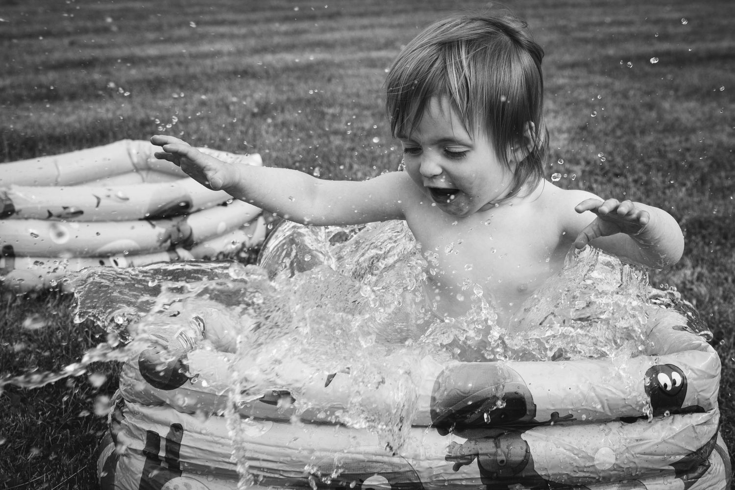 Black and white photo of a small child splashing excitedly in an inflatable pool.