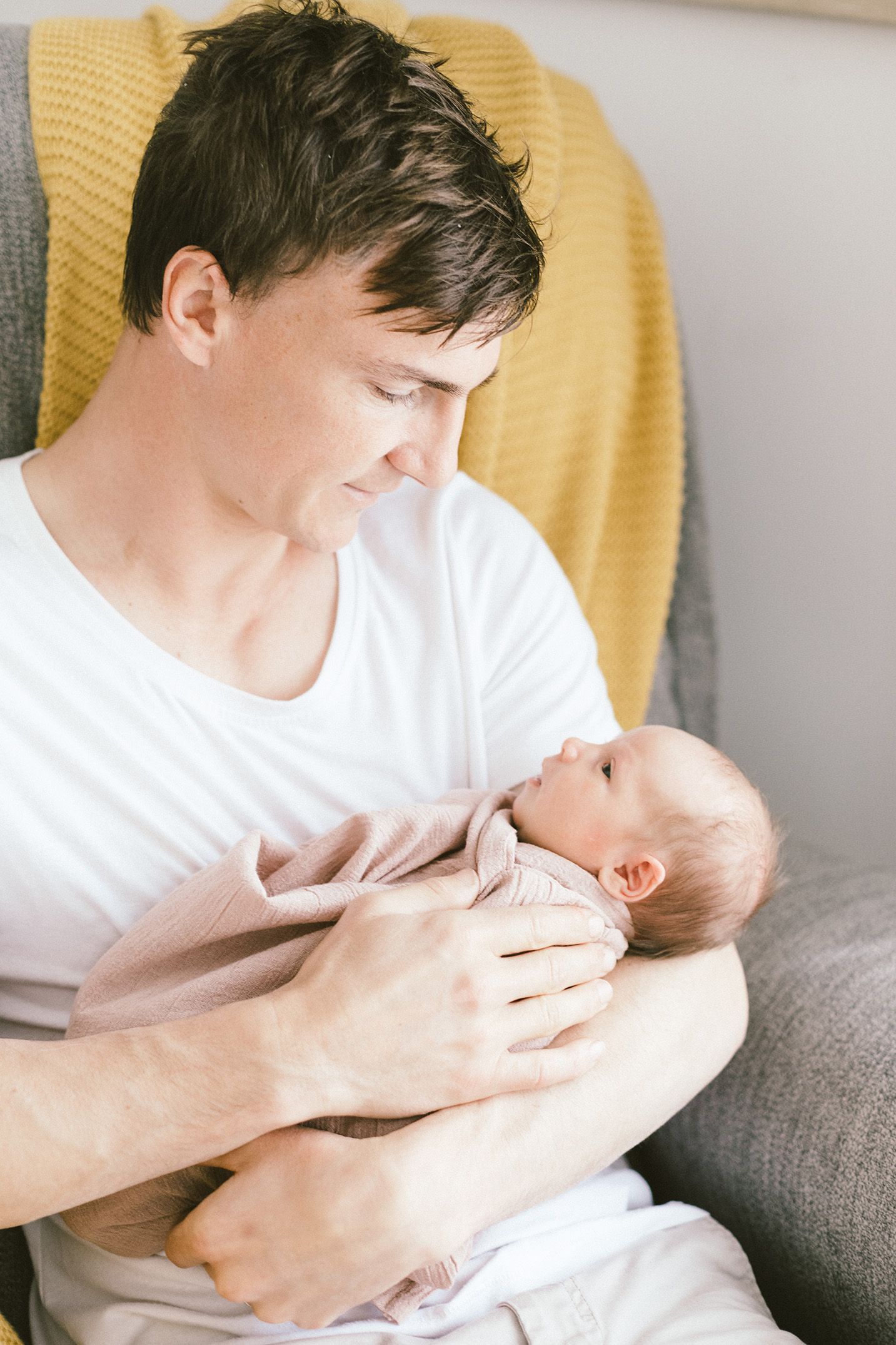 Parent tenderly holding and bonding with newborn baby on yellow chair.