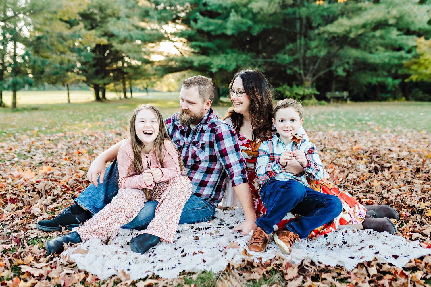 Family sitting on blanket among fall leaves enjoying outdoor time together.