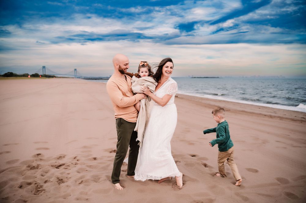 parents holding young daughter while son runs circles around them on South Beach in Staten Island, NY