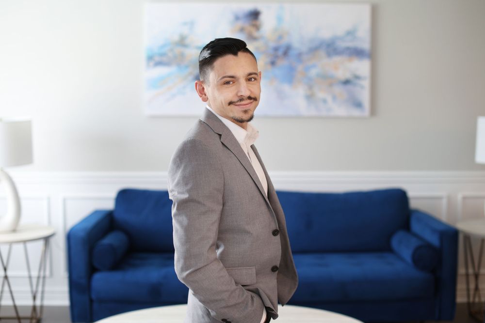 Professional in gray suit jacket standing in modern office with blue couch and abstract art.