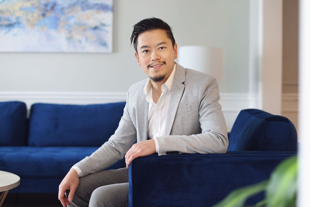 Professional in gray blazer seated on blue couch in modern office setting.