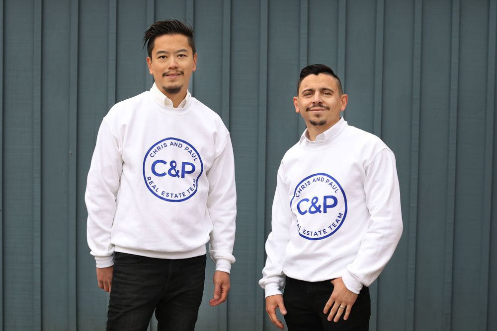 Two people wearing matching white C&P branded sweatshirts standing against gray wall.