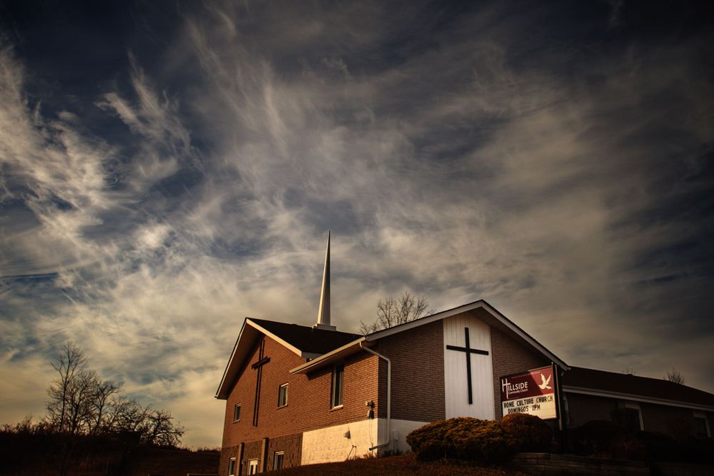 Church building silhouetted against dramatic cloudy sunset sky with cross visible.