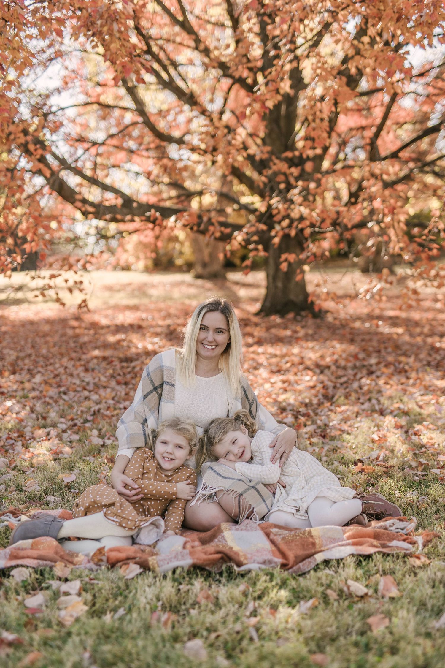 A cozy autumn picnic scene under a large tree with orange leaves on a blanket in a park.