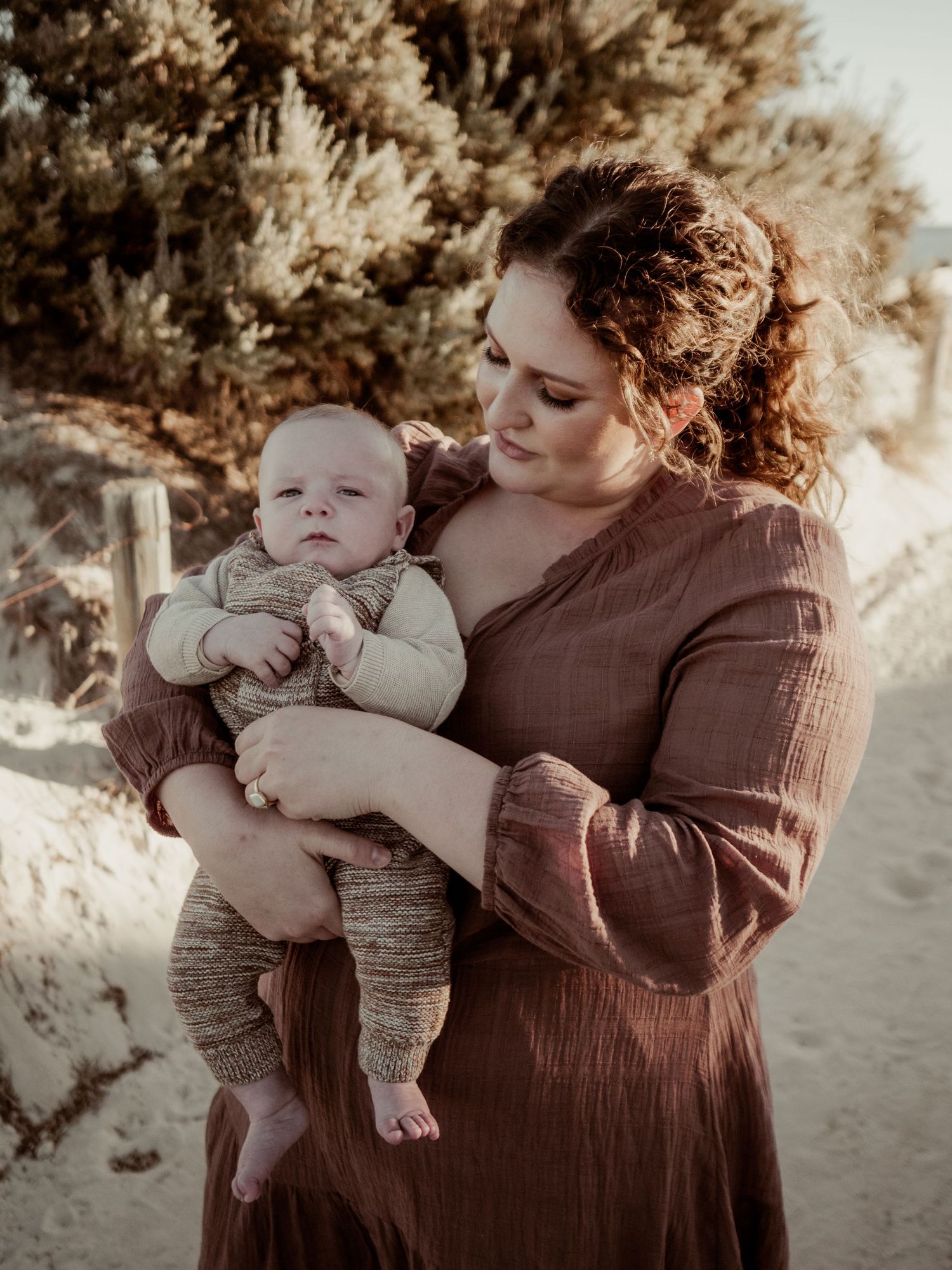 Mother holding newborn baby in her arms whilst at the beach at sunset