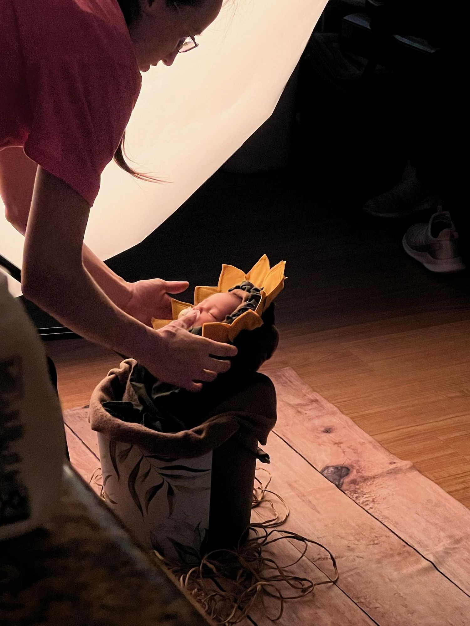 Photographer posing a newborn baby in a sunflower crown inside a burlap sack prop.