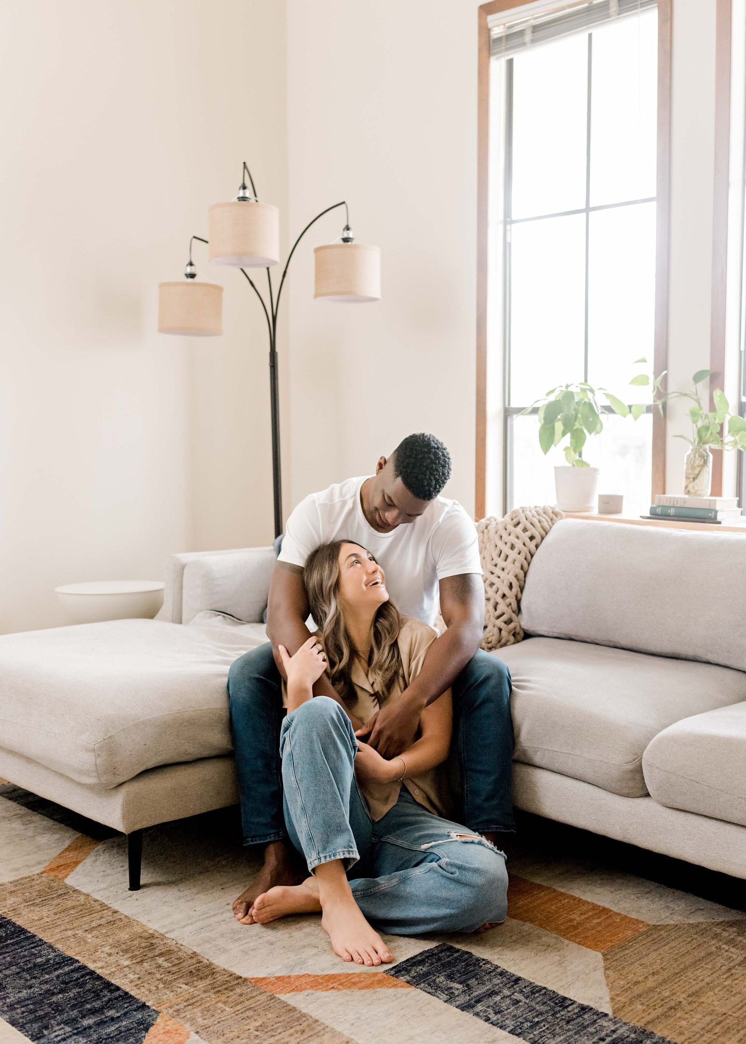 A couple shares a loving moment on their gray sectional sofa beneath a decorative floor lamp.