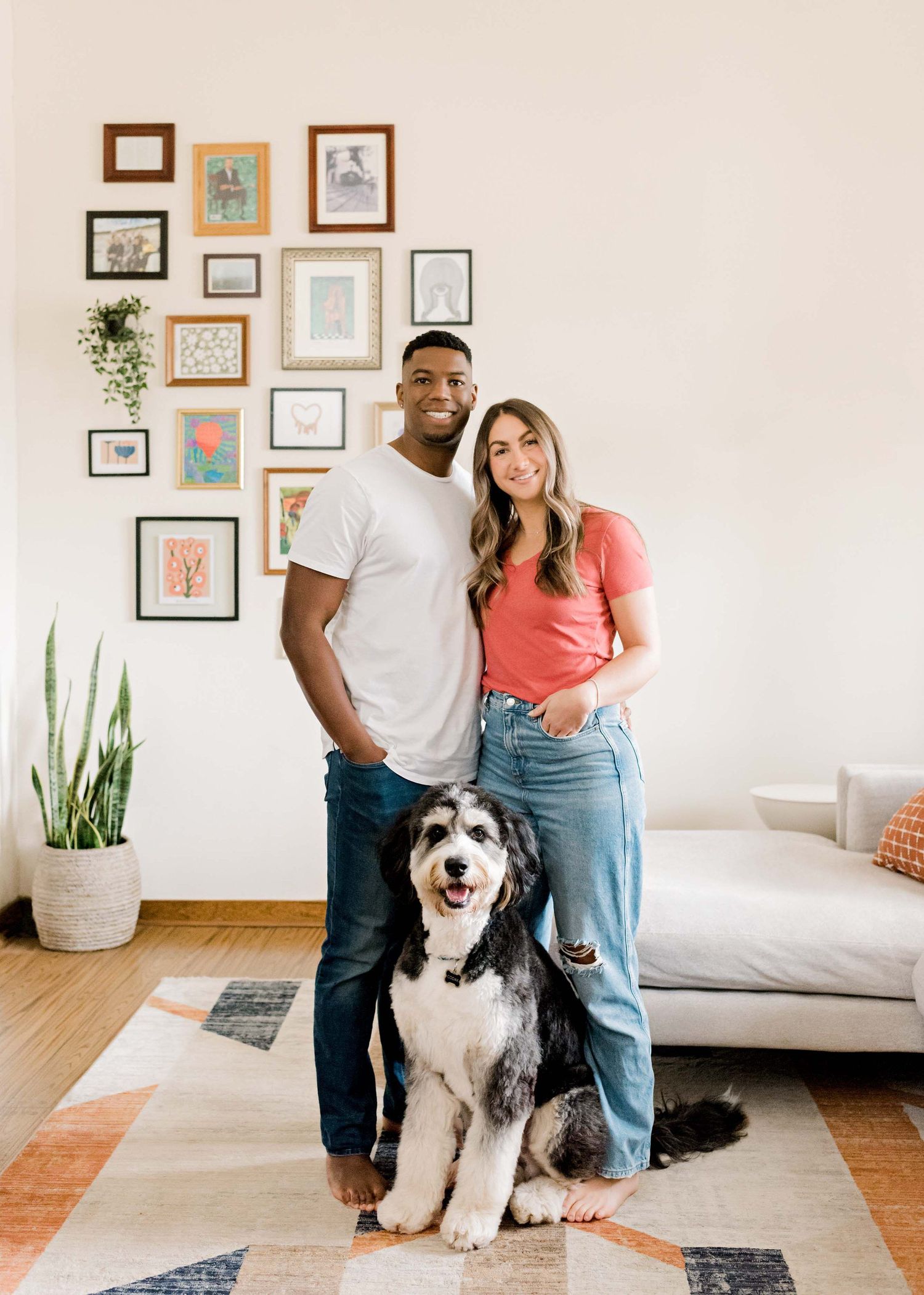 Happy couple poses with their Old English Sheepdog in modern living room with gallery wall.