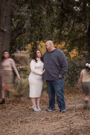 Couple standing on forest path with motion-blurred figures in background.