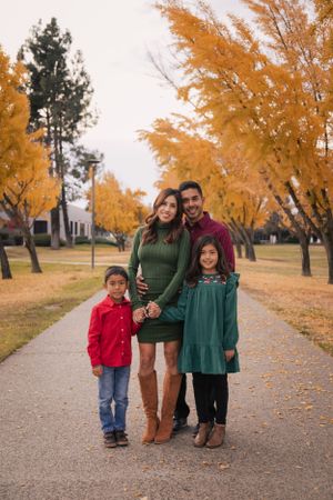 Family of four standing on path lined with golden autumn trees.