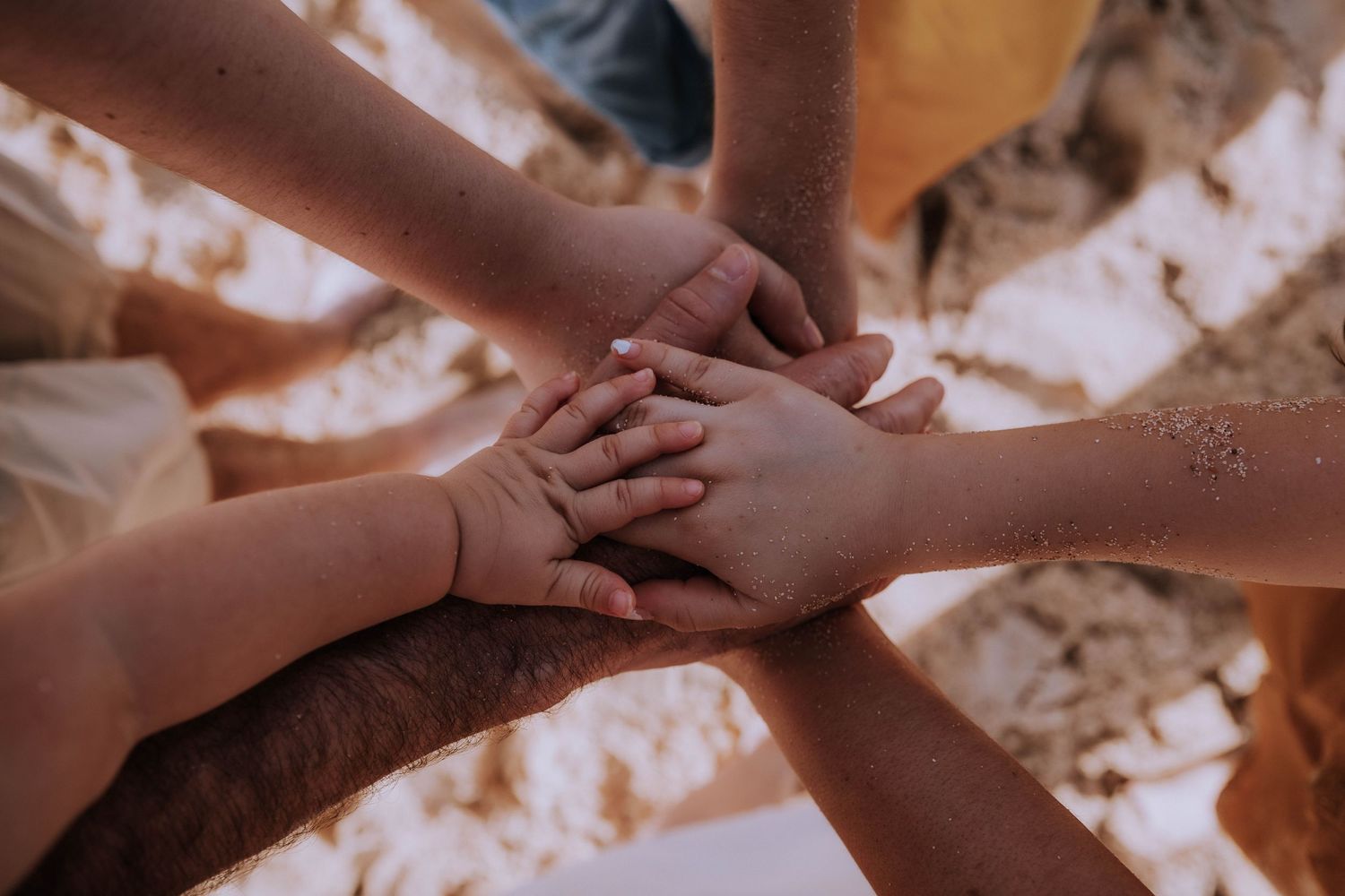 Multiple hands joining together in unity against a warm sunlit background.
