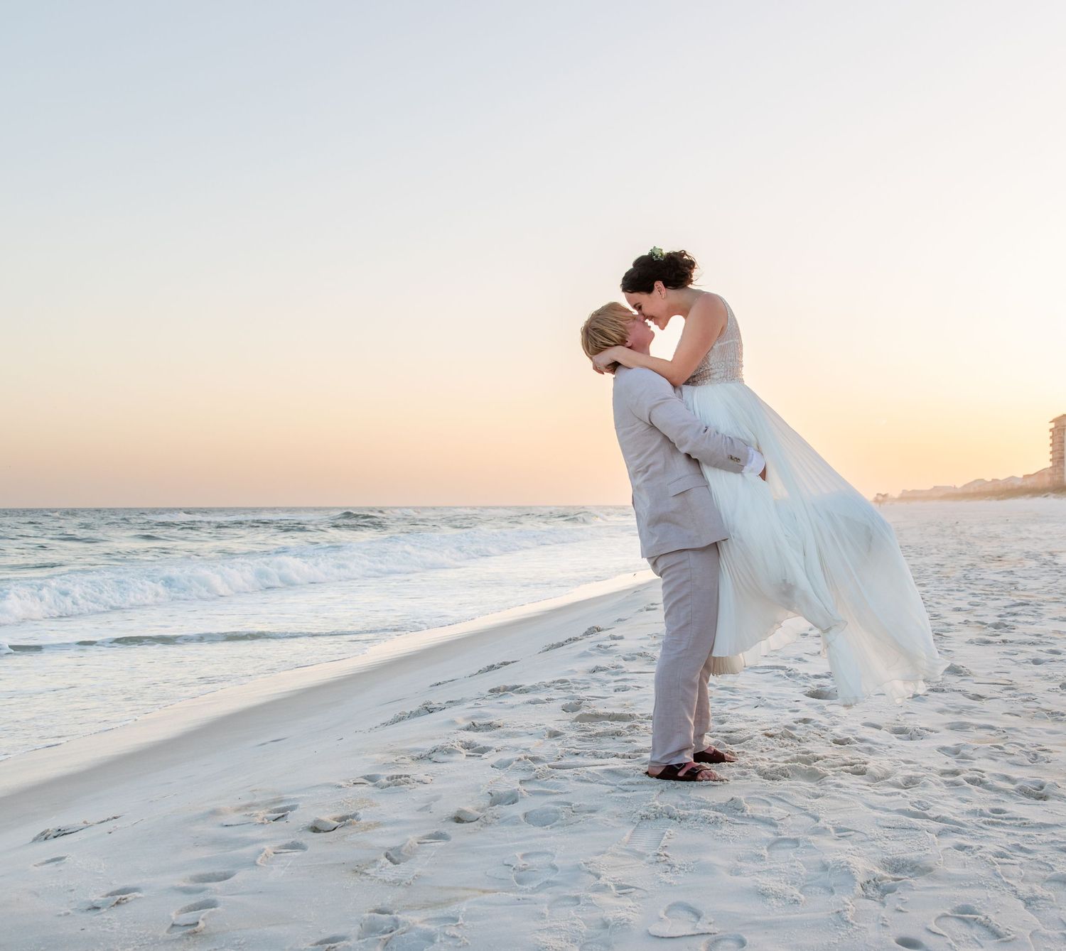 A romantic beach wedding photo with two people embracing against a sunset backdrop.