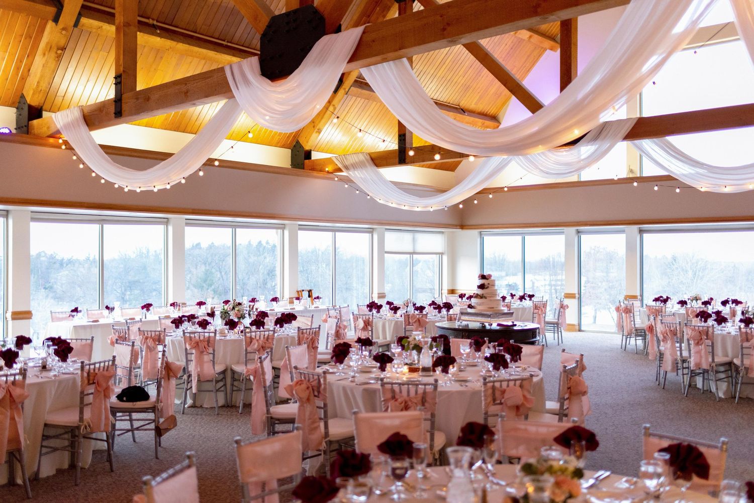 Reception hall decorated with white draping and exposed wooden beams overlooking water view.