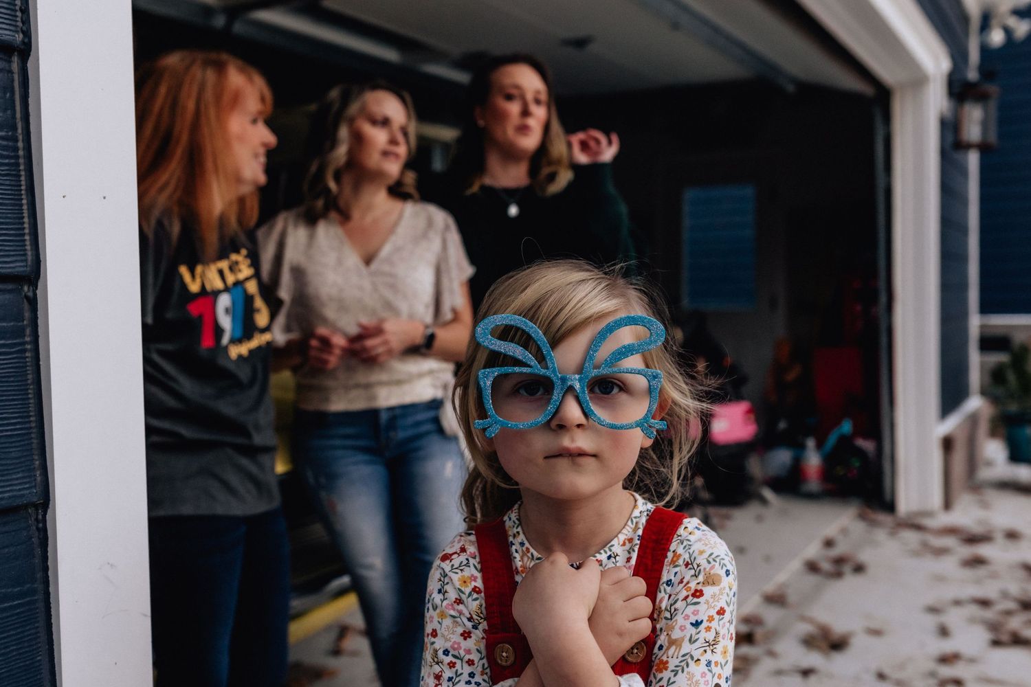 girl with easter bunny glasses standing in front of the garage with aunts and mom behind her in suffolk, virginia