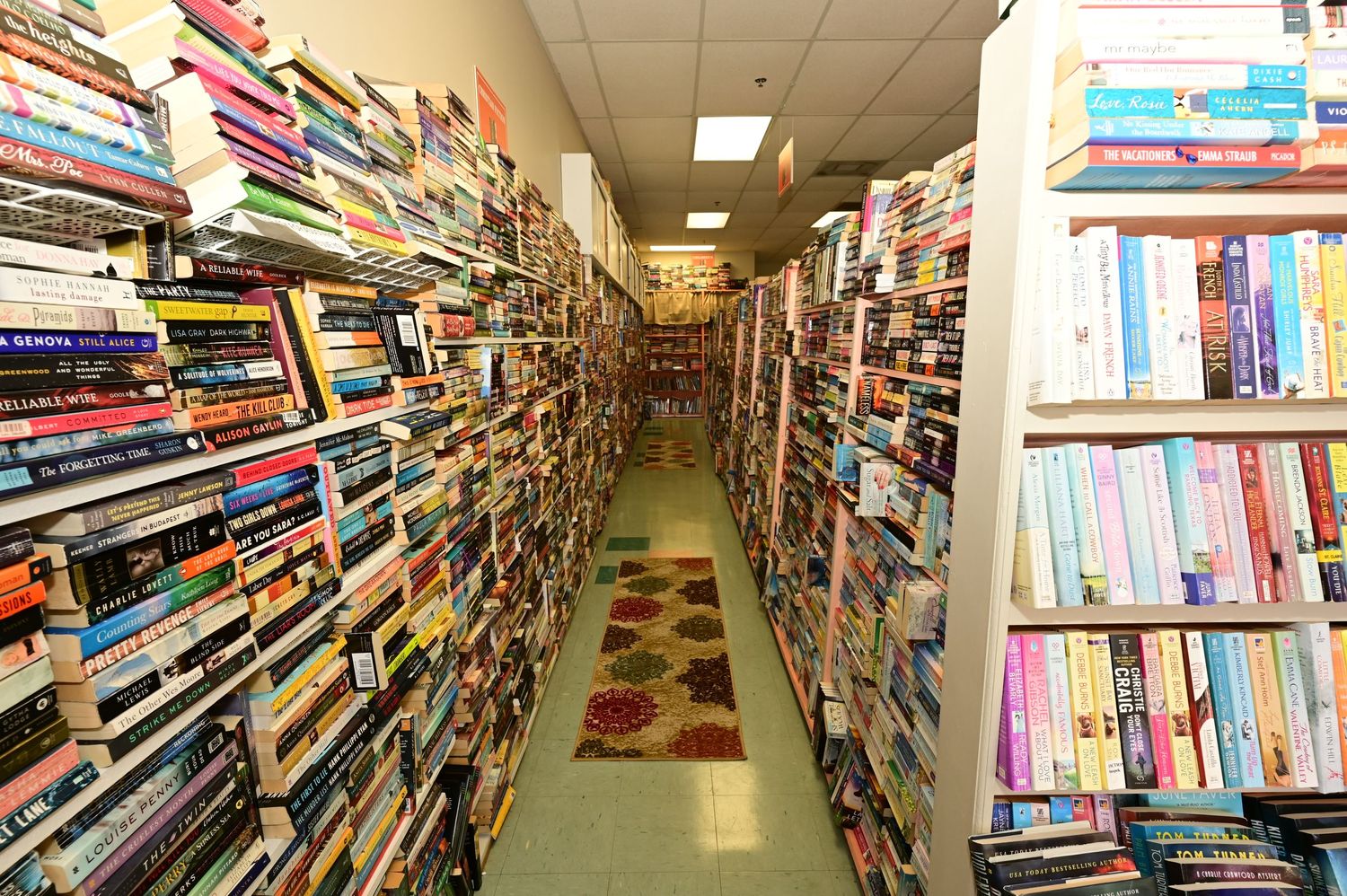 Long aisle view of densely packed bookshelves with colorful spines in used bookstore.