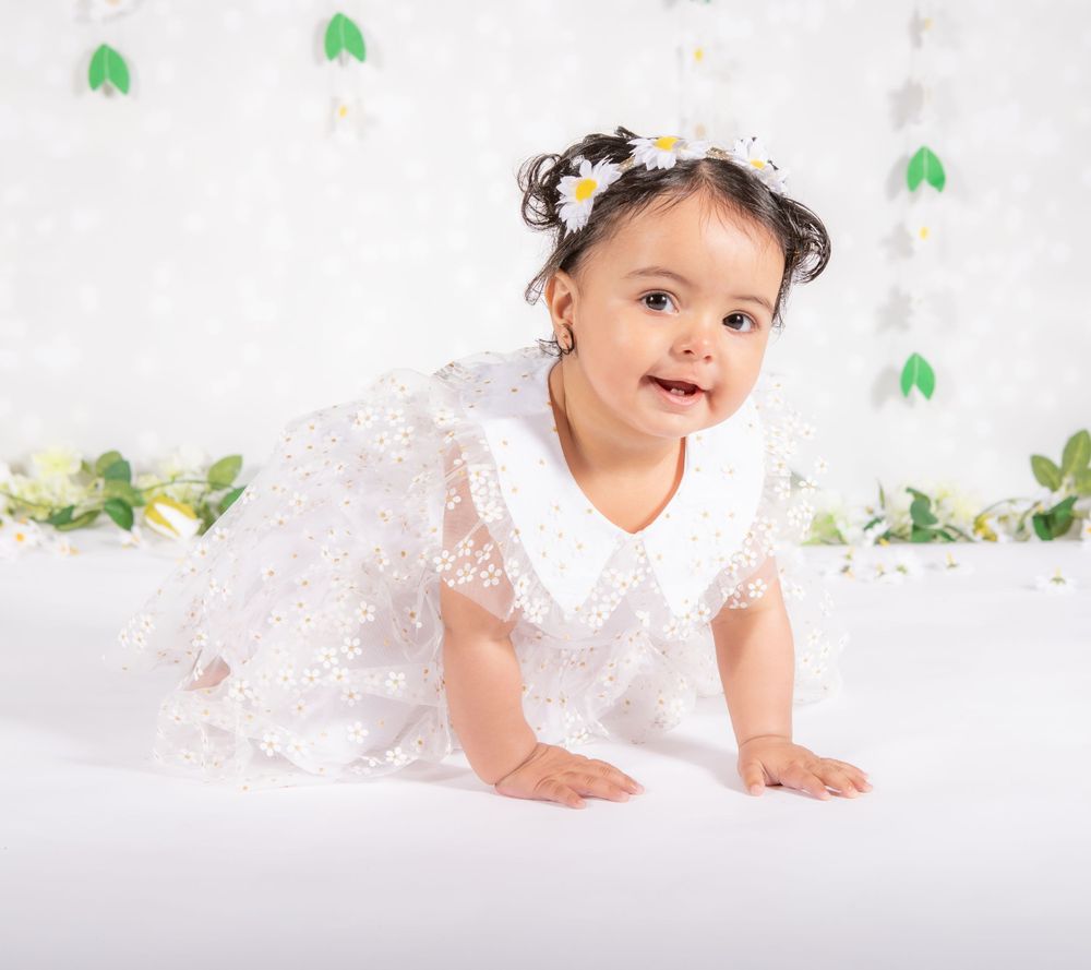 Little girl crawling during a children's photo shoot . Wearing daisies in her hair and a daisy dress. Smiling and happy