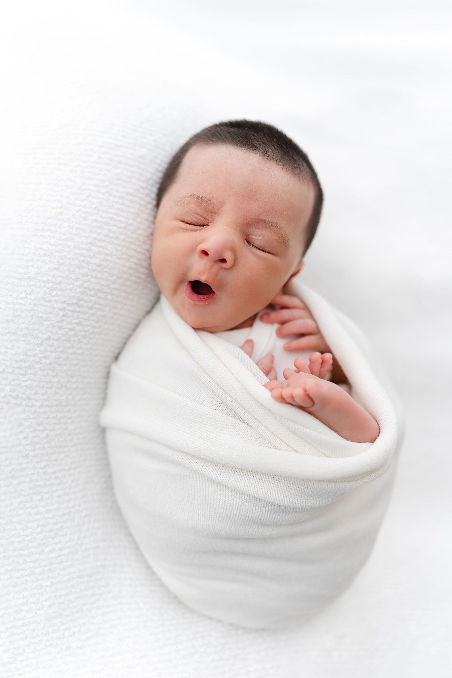 Peaceful newborn baby sleeping while swaddled in white blanket.