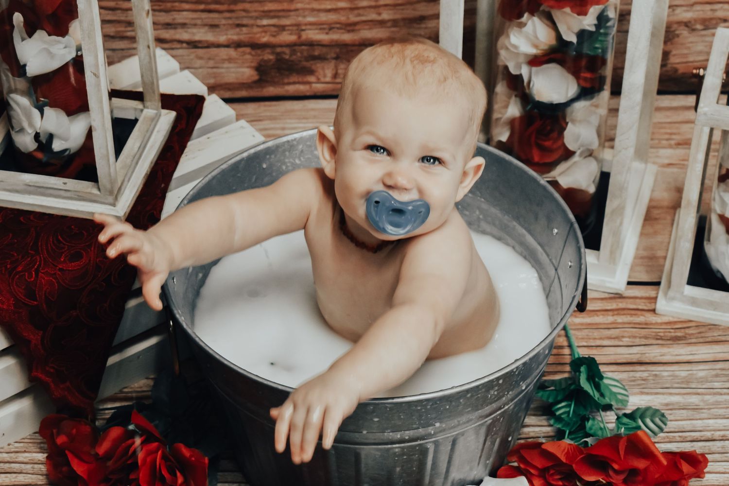 Happy baby with pacifier sitting in galvanized tub with holiday decorations.