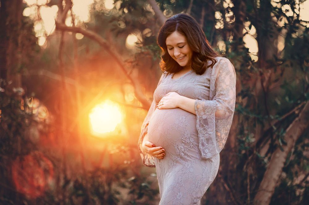 Golden sunset maternity photos taken in a wooded forest setting with soft natural lighting.