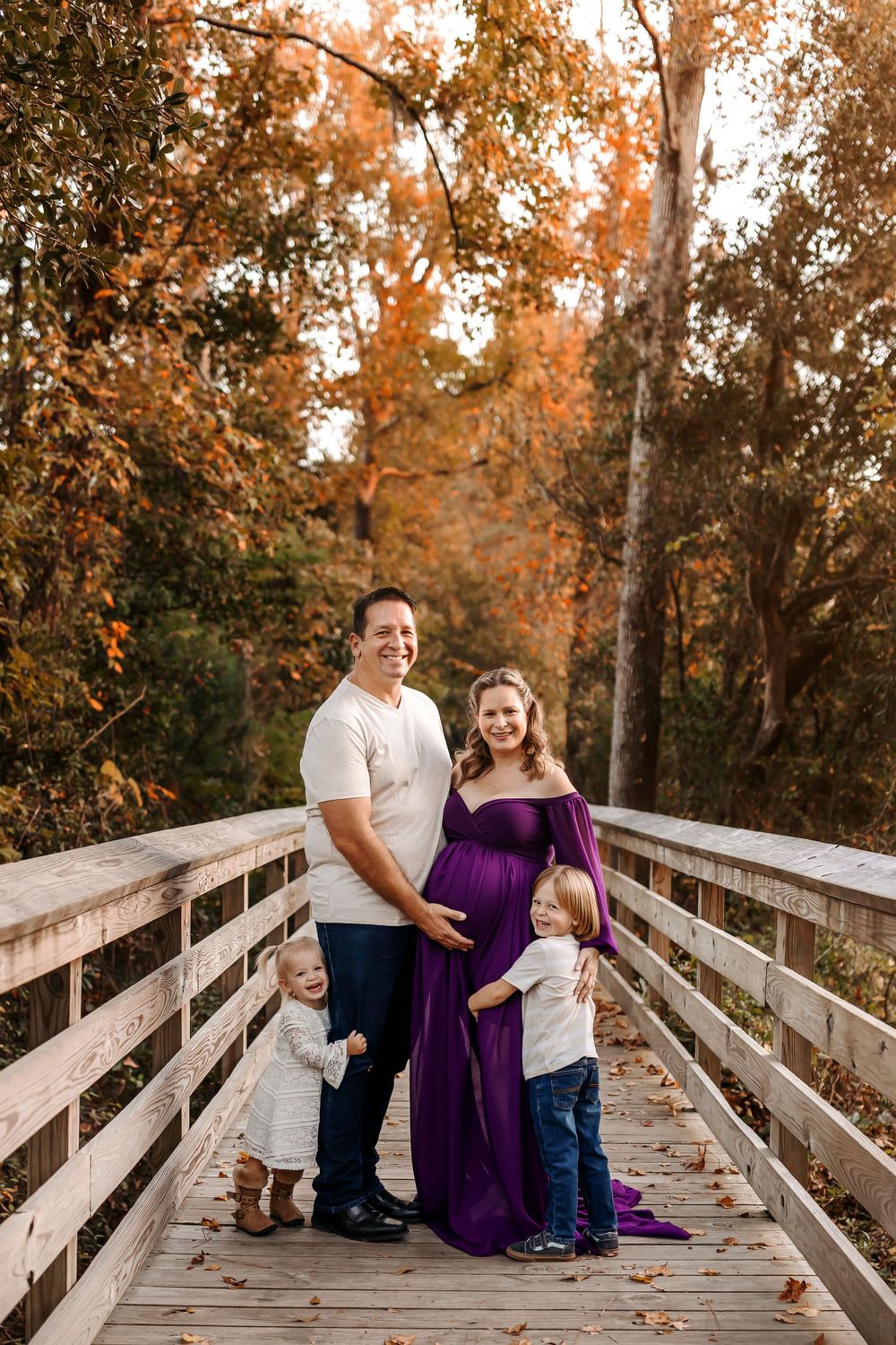 Family photos on a wooden boardwalk surrounded by autumn trees at sunset.