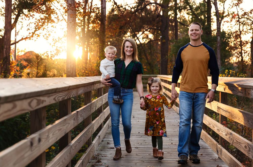 Family walking together on a wooden boardwalk during golden hour with autumn trees in background.