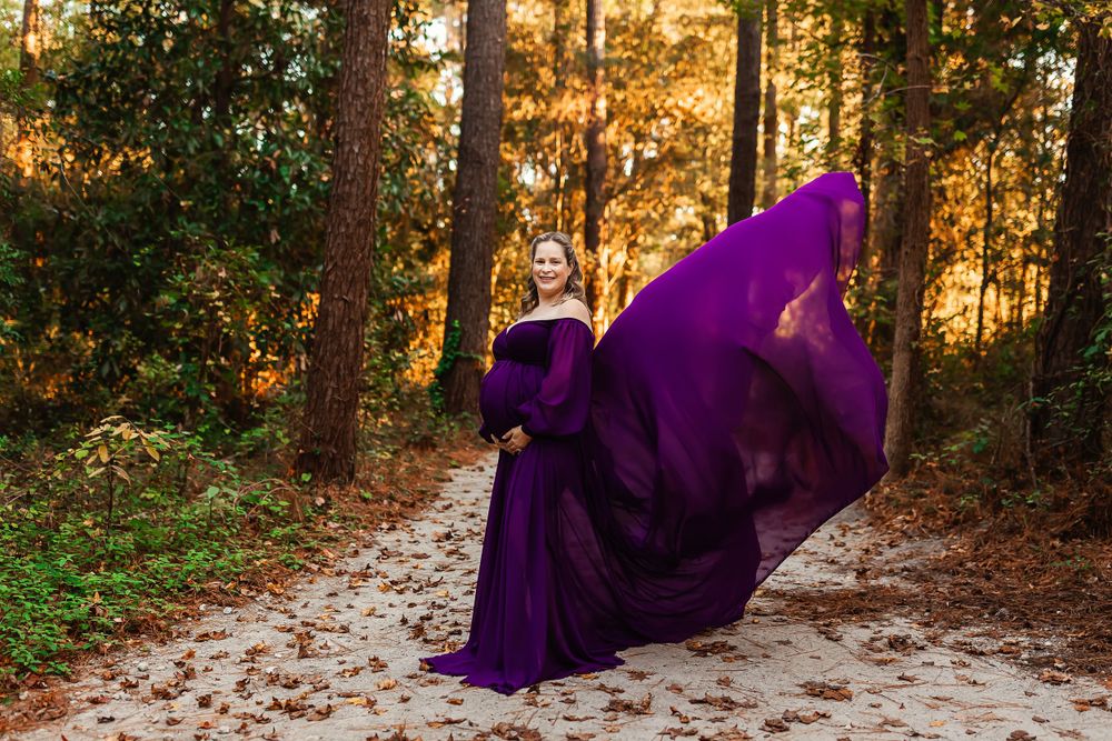 Path through autumn forest with warm golden sunlight filtering through trees and purple dress in frame.