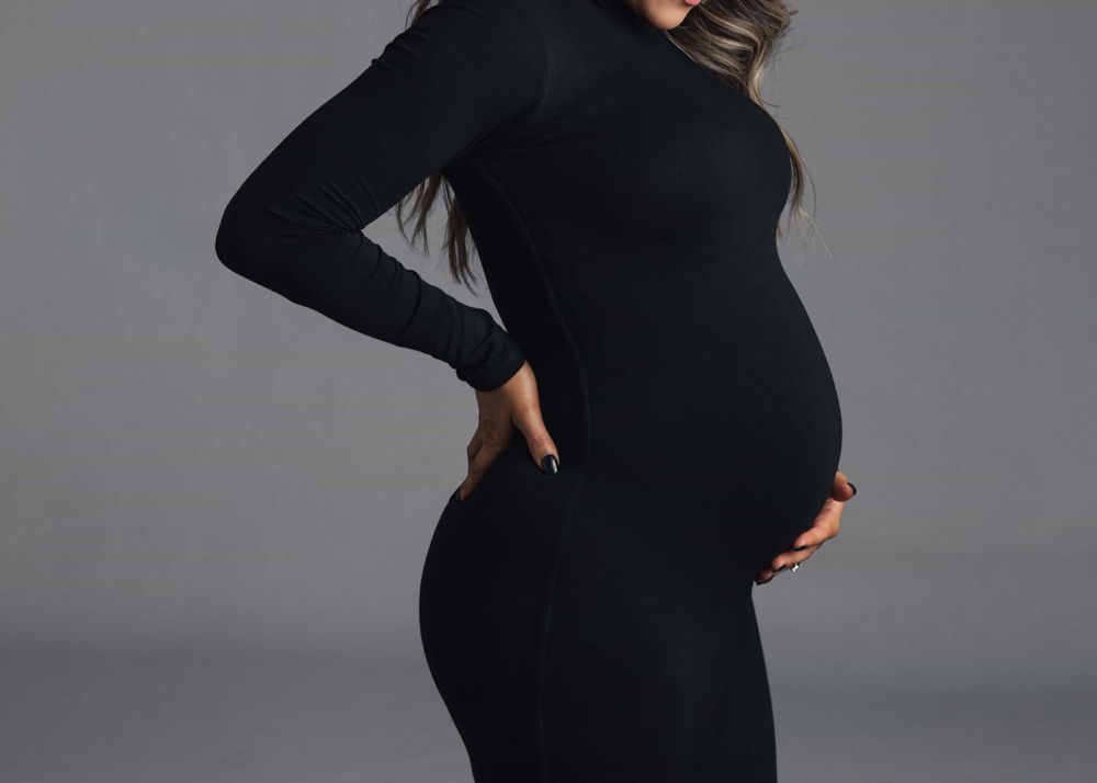 Close-up side view of pregnant woman in black fitted dress showcasing her baby bump in studio.